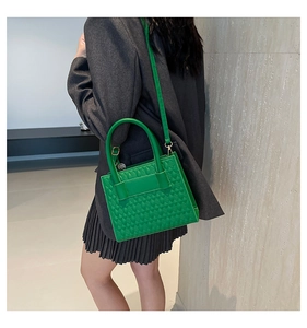 Detail of emerald green box bag with geometric texture worn with a charcoal blazer