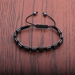 Detail of hand-woven black cord bracelet with dark grey square hematite beads on wood