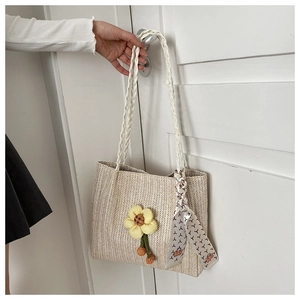 Detail of woven straw tote bag featuring yellow floral charm and patterned silk scarf handle
