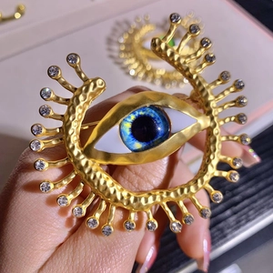Close-up of golden evil eye brooch with blue crystal center and sparkling rhinestones