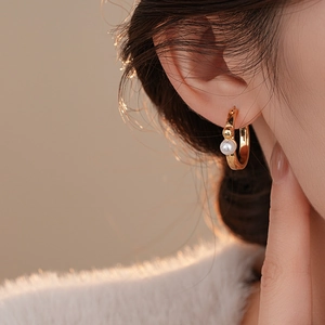 Gros plan détaillé d'une créole en C plaquée or 14 carats avec perle blanche sur le mannequin