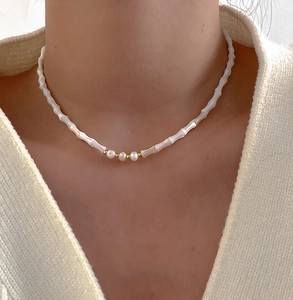 Detail of bamboo shaped beads necklace with white pearls and gold accents on model