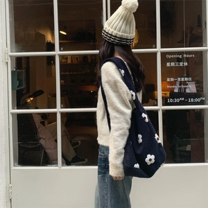 Detail shot of a navy knit tote bag with 3D white flower pattern on a winter outfit