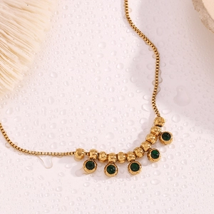 Macro detail of 18K gold plated box chain anklet with green gemstone and steel beads