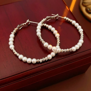 Detailed close-up of beaded hoop earrings with white pearls and silver accents on wood