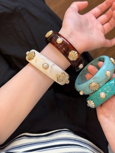 Detail of resin bangle bracelets featuring marble textures, gold shells, and pearl accents