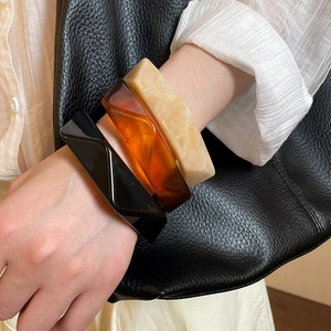 Close-up of resin bracelets in black, amber, and beige marble on a model wrist