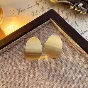 Detailed view of irregular oval earrings with matte brushed gold finish on display tray