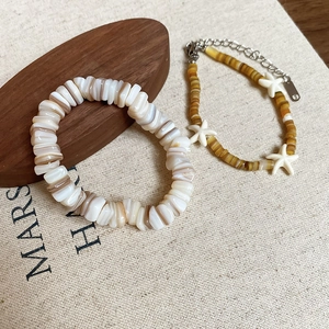 Close-up of shell bead bracelet set with starfish charms on natural canvas background