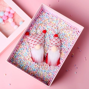 Detail of two handmade Valentine gnomes with heart knit hats in a pink gift box with foam beads