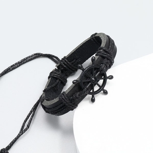 Detail of black woven leather bracelet featuring a vintage metal rudder nautical charm