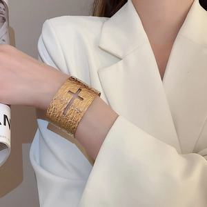 Détail d'un bracelet manchette doré avec croix ajourée et texture martelée porté par un mannequin