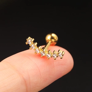 Macro view of gold curved cartilage stud with white zircons held on a fingertip