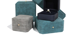 Detail of octagonal dark green and grey jewelry boxes with gold button and pearl ring