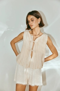 Detail of beige pleated sleeveless top with tie closure and white tassel hem shorts