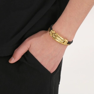 Detail of men's black braided leather bracelet with golden striped metal cylinder clasp