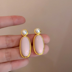 Dettaglio di orecchini dorati con pietre ovali rosa e perle bianche eleganti