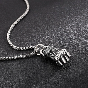 Macro shot of a silver fist pendant with a box chain on a black textured background