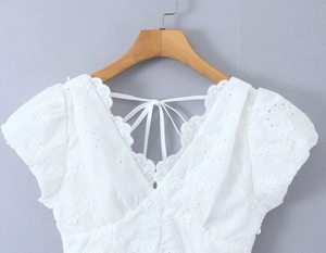 Detalle de blusa blanca con cuello en V, bordado calado intrincado y detalles de encaje