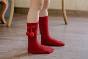 Detail of red ribbed knit baby knee high socks with plush cherry pom-pom decorations