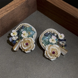 Detail of vintage style earrings with white flowers, blue crystals and pearls in a wooden tray