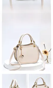 Detail of cream white leather handbag featuring gold hardware and leaf-shaped charm