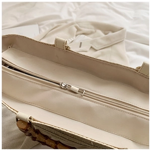 Detail of hand-woven straw tote bag with bamboo handles and secure metal zipper closure
