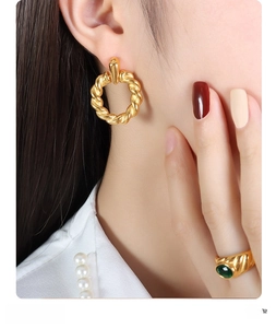 Detailed shot of gold-plated twisted hoop earrings and ring with an oval green gemstone
