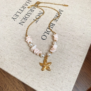 Gold starfish pendant necklace with white pearls and pink shells on a vintage book