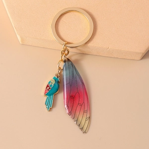 Detailed shot of golden keychain with blue parrot charm and glitter gradient wing pendant