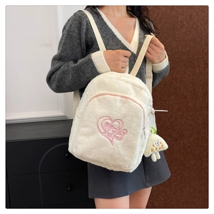 Dettaglio dello zaino in peluche bianco con ricamo a cuore rosa e ciondolo a fungo