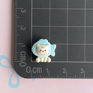 Mini resin bear DIY charm in blue and beige shown on a centimeter scale grid mat