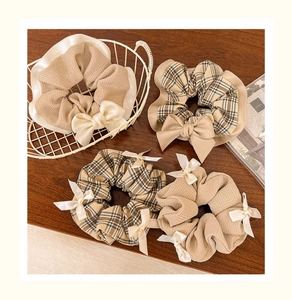 Four-piece set of beige waffle knit and plaid scrunchies with satin bows on wood background