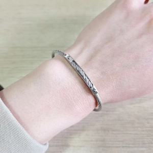 Close-up of a silver braided stainless steel cable bracelet with a rectangular metal plate