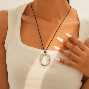Detail of silver circular pendant with black leather cord on model's neckline