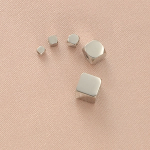 Polished silver stainless steel cube beads with holes on a soft woven texture