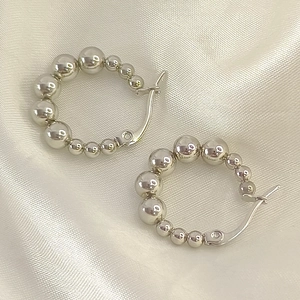 Macro shot of silver beaded hoop earrings with a polished finish on white silk background