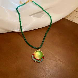 Close-up of green beaded chain with a vintage round resin pendant and colorful stones