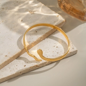 Macro shot of gold snake bracelet showing detailed scale texture on travertine stone