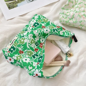 Detailed close-up of green floral makeup bag with black zipper on white fabric