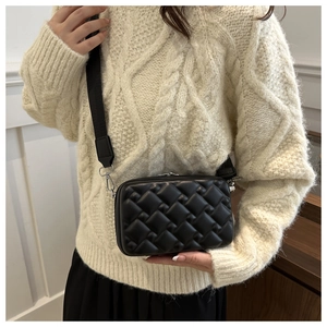 Detail of black quilted shoulder bag with wide nylon strap on white knitted sweater