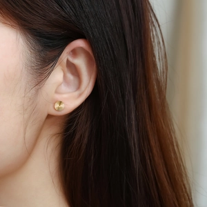 Detail of gold geometric round stud earring with sunburst texture on female model ear