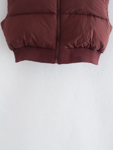 Detail view of the ribbed hem and smooth zipper on a burgundy cropped puffer vest