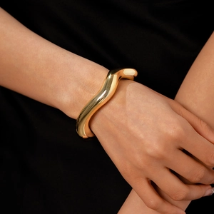 Dettaglio di un ampio bracciale dorato a onde con curve metalliche lucide