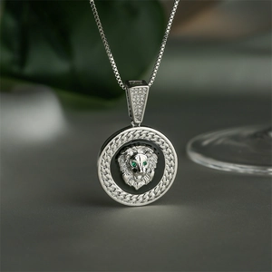 Silver lion head pendant necklace with green gemstone eyes and textured outer ring