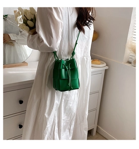 Close-up of green hand-woven bucket bag with drawstring closure on white dress model