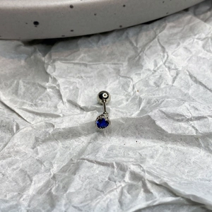 Detail of silver piercing jewelry featuring a pear-shaped dark blue zircon with bead edging