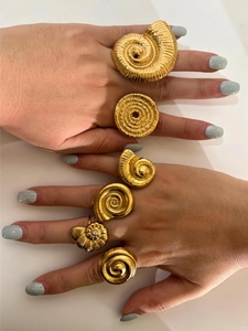 Detail shot of multiple gold-finished conch and shell shaped rings on fingers