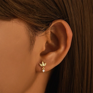 Close-up of gold clover stud earring with clear zircon drop on female earlobe