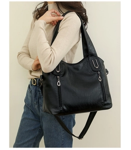 Model wearing a black large capacity leather shoulder bag with decorative metal zippers